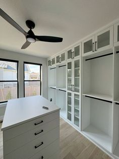 an empty room with white cabinets and a ceiling fan in the corner, next to a window