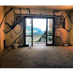 an empty room with graffiti on the walls and open door to another room that has a balcony