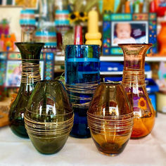 several different colored vases sitting on a table in front of a shelf with other items