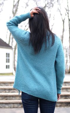 a woman with long hair standing in front of steps wearing a blue sweater and jeans