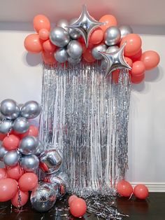 balloons and streamers are on the table in front of a balloon arch with silver and orange balls