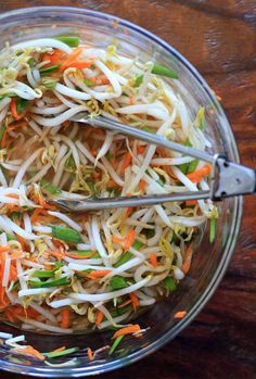 a glass bowl filled with shredded carrots and veggies next to a pair of tongs