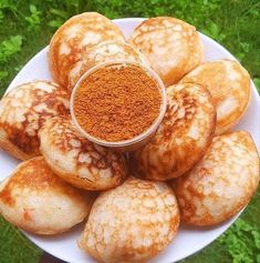 some food on a white plate with a small cup in the middle and green grass behind it