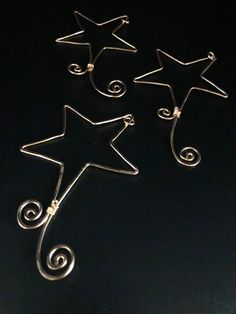 three star shaped earrings sitting on top of a black surface with swirls and spiral designs