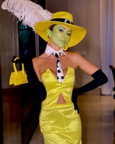 a woman in a yellow dress and hat with feathers on her head is posing for the camera