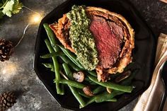 a steak and green beans dish on a black plate next to pine cones, napkins and silverware