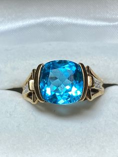 Love blue? This 10K yellow gold ring features a checkerboard faceted cushion cut blue topaz as the star. It measures 10mm x 10mm and secured in a semi bezel mounting. That makes it a 3.5 carat stone. The checkerboard faceting makes it dazzle! Flanking the center stone is are 2 diamond chips in an illusion setting. The ring is a size 8 and weighs in at 4.6 grams. It is a gorgeous ring for any occasion! Swirl Diamond Ring, Gorgeous Ring, White Gold Diamond Rings, Love Blue, Yellow Gold Ring, Gold Diamond Rings, Diamond Sizes, Topaz Ring, Cushion Cut