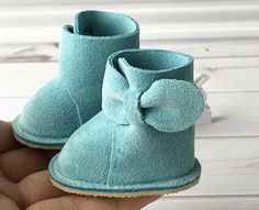 a hand is holding a pair of blue baby boots with bows on the front and side