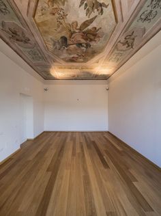 an empty room with wood flooring and painted murals on the ceiling, along with white walls