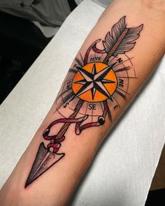 a compass tattoo on the arm with an orange and black arrow next to it,