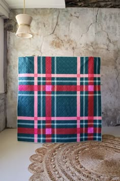 a blue and pink plaid blanket sitting on top of a rug next to a lamp