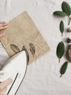 someone is ironing something on a piece of paper with leaves and mushrooms around it