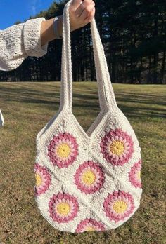 a crocheted bag with pink and yellow flowers on the front is held up by a woman's hand