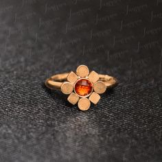 a gold ring with an orange stone in the center on a black surface and words written below it