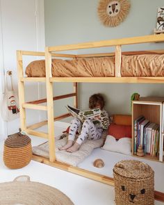 a young child sitting on top of a bunk bed next to a basket and bookshelf