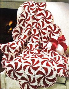 a red and white afghan sitting on top of a chair next to a fireplace with a bow