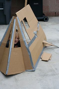 a young boy sitting in a cardboard box on the ground with his head sticking out