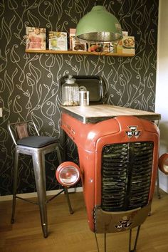 an old car is sitting in front of a wall with pictures on it and two stools