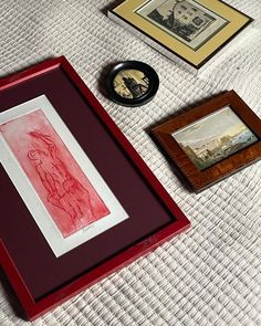 three framed pictures on a bed next to a clock and other art work in frames