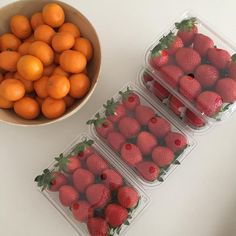 four plastic containers filled with strawberries next to a bowl of oranges