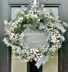 a christmas wreath on the front door with white flowers and greenery hanging from it