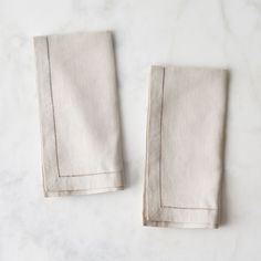 two linen napkins with stitching on them sitting on a marble countertop top