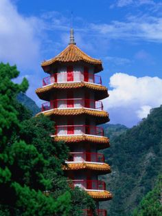 a tall tower with red balconies in front of some trees and mountains behind it