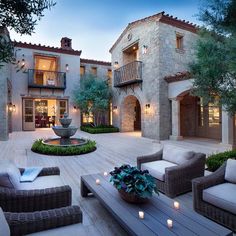 an outdoor living area with couches and tables in front of a large house at dusk