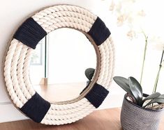 a white rope wreath sitting on top of a wooden floor next to a potted plant