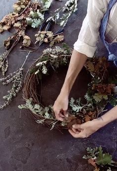 a person is making a wreath out of branches and leaves on the ground with scissors