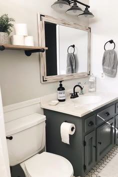 a white toilet sitting under a bathroom mirror next to a wooden sink vanity with two rolls of toilet paper on top of it