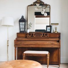 a living room with a piano, ottoman and mirror on the wall in front of it