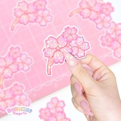 a hand holding a pink flower sticker over a pink background with flowers on it