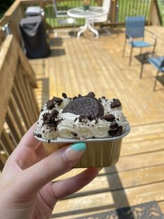 a person holding up a cupcake with white frosting and oreo cookies on it