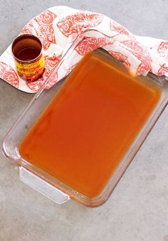 a glass container filled with orange liquid next to a napkin and a cup of coffee