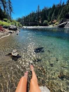 a person's feet in the water near rocks and trees