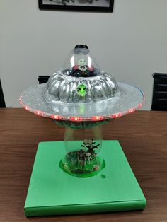 an alien spaceship model sitting on top of a green box with red lights around it