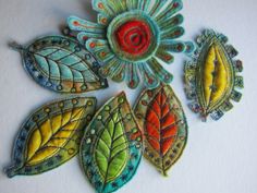 four different colored leaf shaped brooches on a white surface