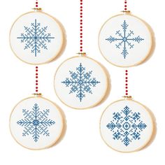 three cross stitch snowflakes hanging from strings on a white wall with red beads