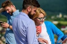 two men and a woman looking at something on their cell phones while standing next to each other