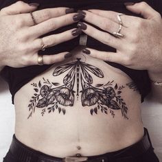 a woman's stomach with flowers and leaves tattooed on the side by her hands