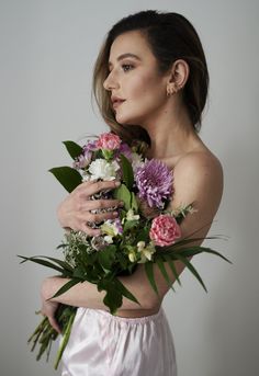 a woman in a white dress holding a bouquet of flowers with her arm wrapped around her shoulder