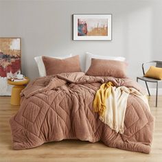 a bed covered in a brown comforter next to a chair and painting on the wall