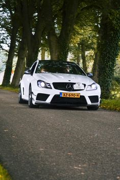 a white car parked on the side of a road next to some trees and bushes