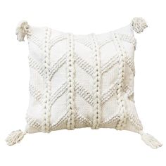 a white knitted pillow with tassels on the front and back, sitting on top of a white surface