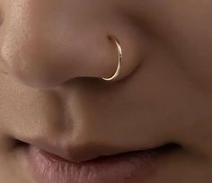 a woman's nose with a gold nose ring on her left side, and an open nose piercing in the middle