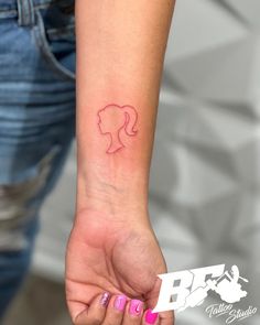 a woman's hand with a small pink tattoo on her left wrist and the outline of a female head