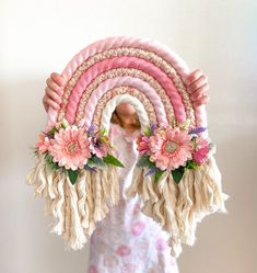 a woman holding up a pink and white decorative object with flowers on it's sides