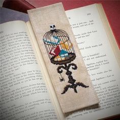 a cross stitch bookmark with a bird in a cage on top of an open book