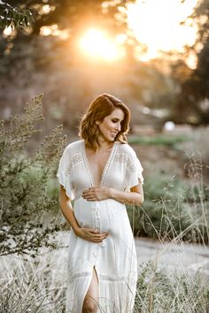 a pregnant woman standing in tall grass at sunset